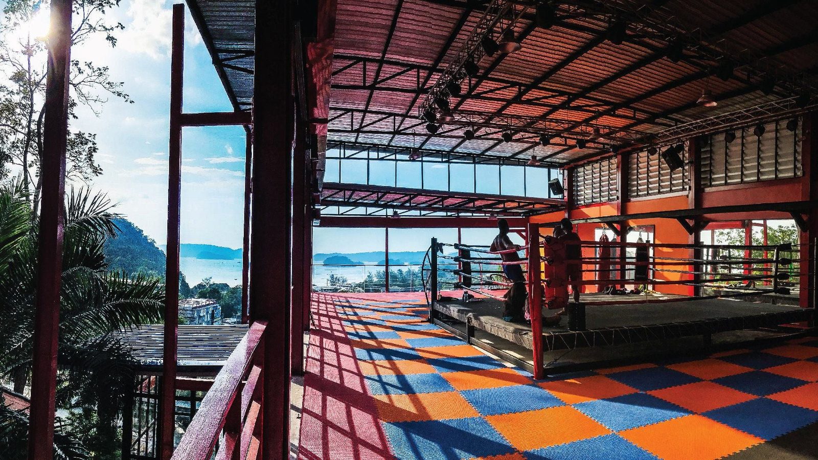 Khun Suek Muay Thai rings and training floor in Ao Nang, with limestone mountains and the Andaman Sea beyond.